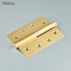 May include: A brass door hinge with a cylindrical barrel and rectangular leaves. Each leaf has multiple screw holes. The word "Vision" is printed in the upper left corner. The hinge is a warm gold colour.