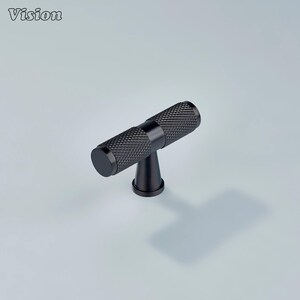May include: A black T-bar cabinet pull with a textured, diamond-patterned grip. The hardware features a cylindrical handle and a short, conical base. The word "Vision" is in the upper left corner.