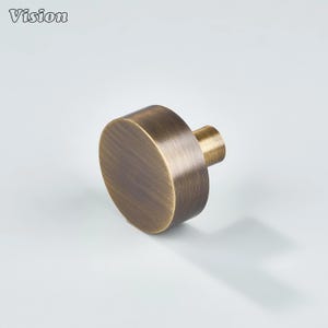 May include: A bronze-colored cabinet knob with a cylindrical body and a short, rounded stem. The knob has a brushed metal finish and is designed for furniture. The word "Vision" is in the top left corner.