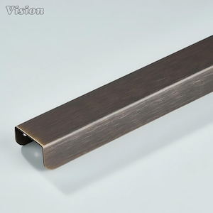 May include: A bronze-coloured metal trim piece with a rectangular profile. The trim has a slightly curved edge and a brushed finish, with the word "Vision" in the upper left corner. The metal has a warm, antique appearance.
