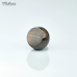 May include: A bronze-colored, spherical cabinet knob with a flat, circular face. The knob has a brushed metal texture and a reflective surface. The word "Vision" is in the upper left corner.