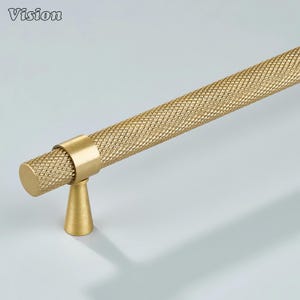 May include: A gold-toned cabinet handle with a diamond-patterned grip. The handle has a cylindrical bar and a conical base. The word "Vision" is in the upper left corner. Suitable for kitchen or bathroom cabinets.