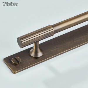 May include: Bronze door pull with a cylindrical handle and horizontal grooves. The pull is mounted on a rectangular plate with a screw head. The word "Vision" is in the upper left corner. Suitable for doors and cabinets. Measurements are in centimetres.