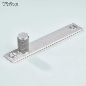 May include: A brushed metal door pull featuring a cylindrical handle with a diamond-patterned grip and a rectangular base. Two screws secure the base. The word "Vision" is in the upper left corner.