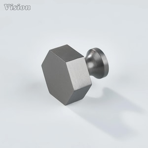 Könnte beinhalten: Ein schiefergrauer Schrankknauf mit einem geometrischen, sechseckigen Design. Der Knauf hat einen zylindrischen Sockel und einen facettierten, sechseckigen Hauptkörper. Das Wort "Vision" befindet sich in der oberen linken Ecke.