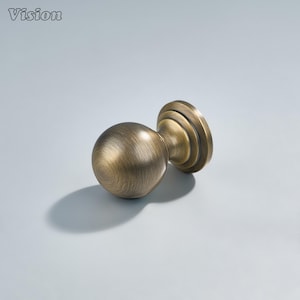 May include: A bronze-colored cabinet knob with a spherical handle and a circular base. The knob has a textured surface and is designed for furniture. The word "Vision" is in the top left corner.