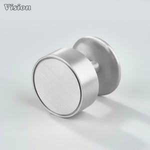 Puede incluir: Un pomo de armario de metal cepillado con un diseño circular. El pomo tiene un cuerpo cilíndrico y una base redonda. La palabra "Vision" está en la esquina superior izquierda. El pomo es de metal color plata.