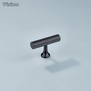 May include: A black T-bar cabinet pull. The horizontal bar features a ridged texture, and the base is smooth and rounded. The word "Vision" is visible in the upper left corner.