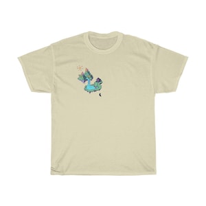 May include: A cream-colored t-shirt featuring a colorful graphic of a fantasy island with a waterfall, sun, and moon. The island has a small house and a waterfall. The design is in shades of blue, green, and purple.