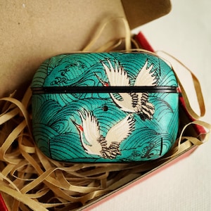 Peut inclure: Un étui turquoise avec un motif d'inspiration japonaise représentant des grues blanches avec des accents rouges et un motif de vagues. L'étui est dans une boîte rouge avec des lanières de papier brun.