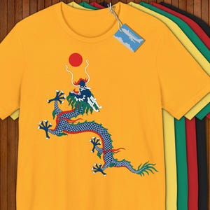 May include: Mustard yellow t-shirt featuring a detailed illustration of a blue and red dragon with a red sun. The dragon design is centered on the shirt. Additional shirts in various colors are stacked behind the main shirt.