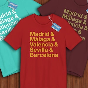 May include: Three t-shirts in teal, red, and burgundy, each displaying city names in a stacked format. The red shirt prominently features "Madrid & Málaga & Valencia & Sevilla & Barcelona" in gold lettering. Each shirt has a tag.