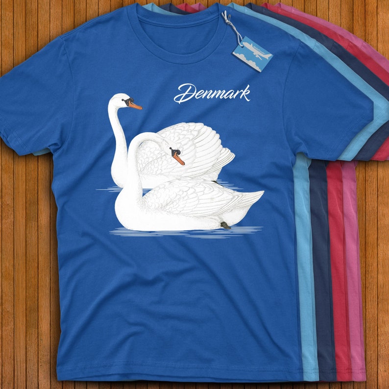 May include: A royal blue t-shirt with a white graphic of two swans on a blue lake. The text "Denmark" is printed in black cursive above the swans.