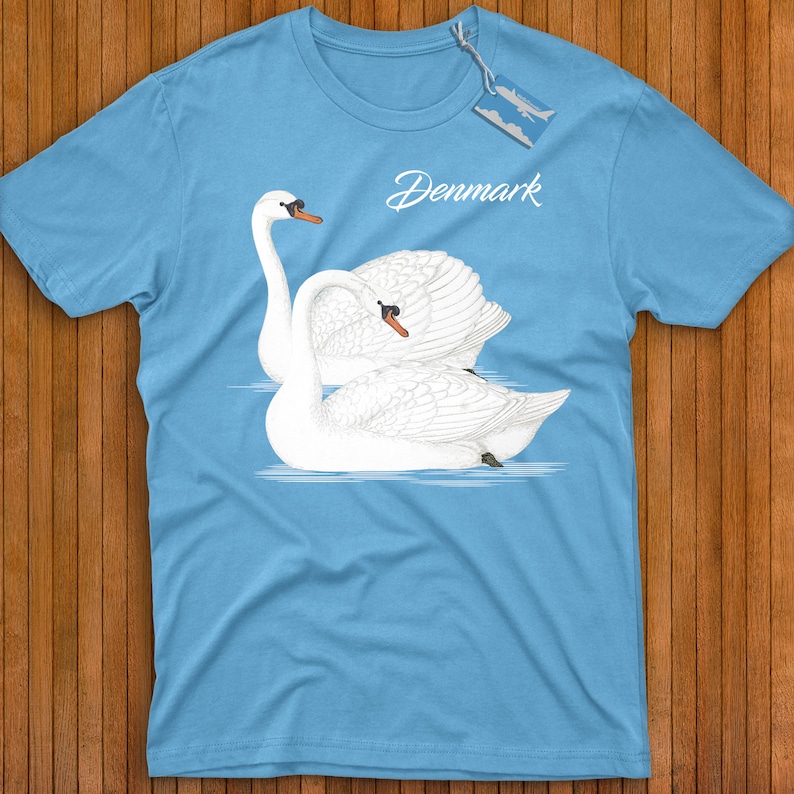 May include: A light blue t-shirt with a graphic of two white swans on a blue background. The text "Denmark" is printed in black on the shirt.