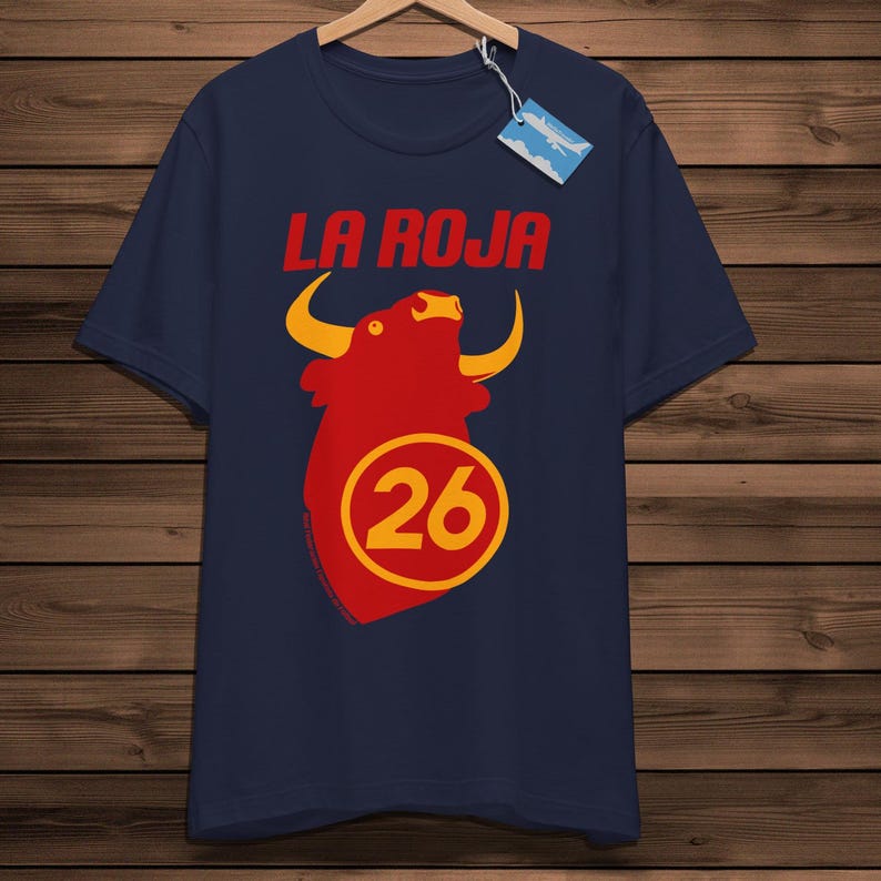 May include: Navy blue t-shirt featuring the red text "LA ROJA" above a red bull graphic with yellow horns. A yellow circle with the number 26 is below the bull.