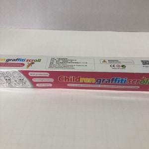 May include: A pink and white box with the text "Children graffiti scroll" on it. The box contains a white scroll with a grid pattern. The scroll is designed for children to draw on without making a mess. The box also has the text "Stick on walls without pollution Easy section with tooth portion design" on it.