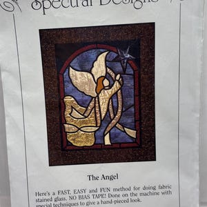 May include: A Spectral Designs fabric stained glass pattern titled "The Angel." The design features an angel with gold wings and a star, set against a blue and red background. The package includes step-by-step photos and instructions.