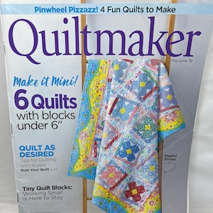 May include: A colorful quilt displayed on a wooden rack, featured on the cover of "Quiltmaker" magazine. The quilt has a floral pattern with blue, red, and yellow accents. The magazine cover includes text: "Pinwheel Pizzazz! 4 Fun Quilts to Make" and "Make it Mini! 6 Quilts with blocks under 6".