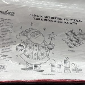 May include: A plastic-wrapped craft kit for a Christmas table runner and napkins. The design features a pixelated Santa Claus holding a star wand, gifts, and snowflakes. The kit includes a color chart and instructions.