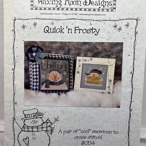 May include: A cross-stitch pattern titled "Quick 'n Frosty" featuring two framed snowman designs. One says "chillout" and the other says "Will Work for Freezer Space." The pattern includes a drawing of a snowman and the text "A pair of "cool" snowmen to cross stitch! #054."