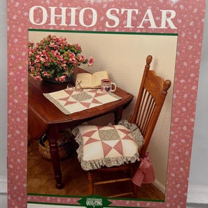 May include: A book cover titled "SUPER SIMPLE QUILTS #2 OHIO STAR" featuring a photo of a quilt, chair, and table setting. The book cover has a pink floral pattern. The author's name, Kathleen Eaton, is at the bottom.