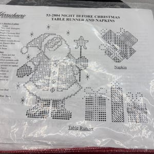 May include: A cross-stitch kit for a Christmas table runner and napkins. The design features Santa Claus, presents, and stars. The kit includes instructions and materials for creating a festive holiday table setting.