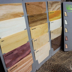 May include: A sample wood card display with different wood types, including cherry, maple, and cedar. The cards are arranged in a grid pattern and labeled with the type of wood. The display is made of gray cardboard and has a small logo for "Cards of Wood" in the upper right corner.