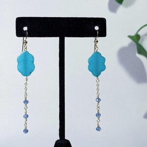 May include: A pair of turquoise flower-shaped dangle earrings with a gold chain and blue crystal accents.