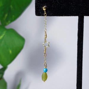 Può includere: Orecchini pendenti dorati con una pietra preziosa verde e blu e un ciondolo a forma di stella.