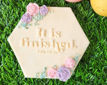 May include: White hexagonal ceramic tile with the text "It is finished. John 19:30" and pastel pink and purple flowers.