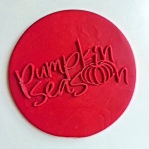 Op de afbeelding: Ronde rode stempel met de tekst "Pumpkin Season" in wit handschrift met een gestileerde pompoen afbeelding.