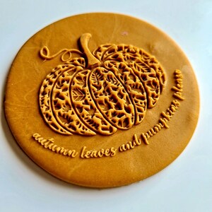 Op de afbeelding: Een ronde, goudkleurige stempel met een gedetailleerd ontwerp van een pompoen met bladeren en de tekst "autumn leaves and pumpkins please".