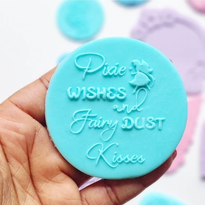 以下が含まれることがあります： 妖精のシルエットが描かれた、薄い青色のシリコンスタンプ。"Pixie Wishes and Fairy Dust Kisses"という文字が刻まれています。