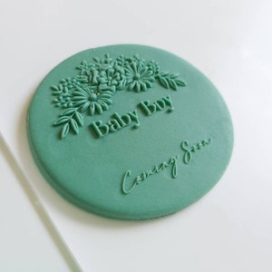 May include: A green round cake topper with a floral design and the text "Baby Boy Coming Soon".