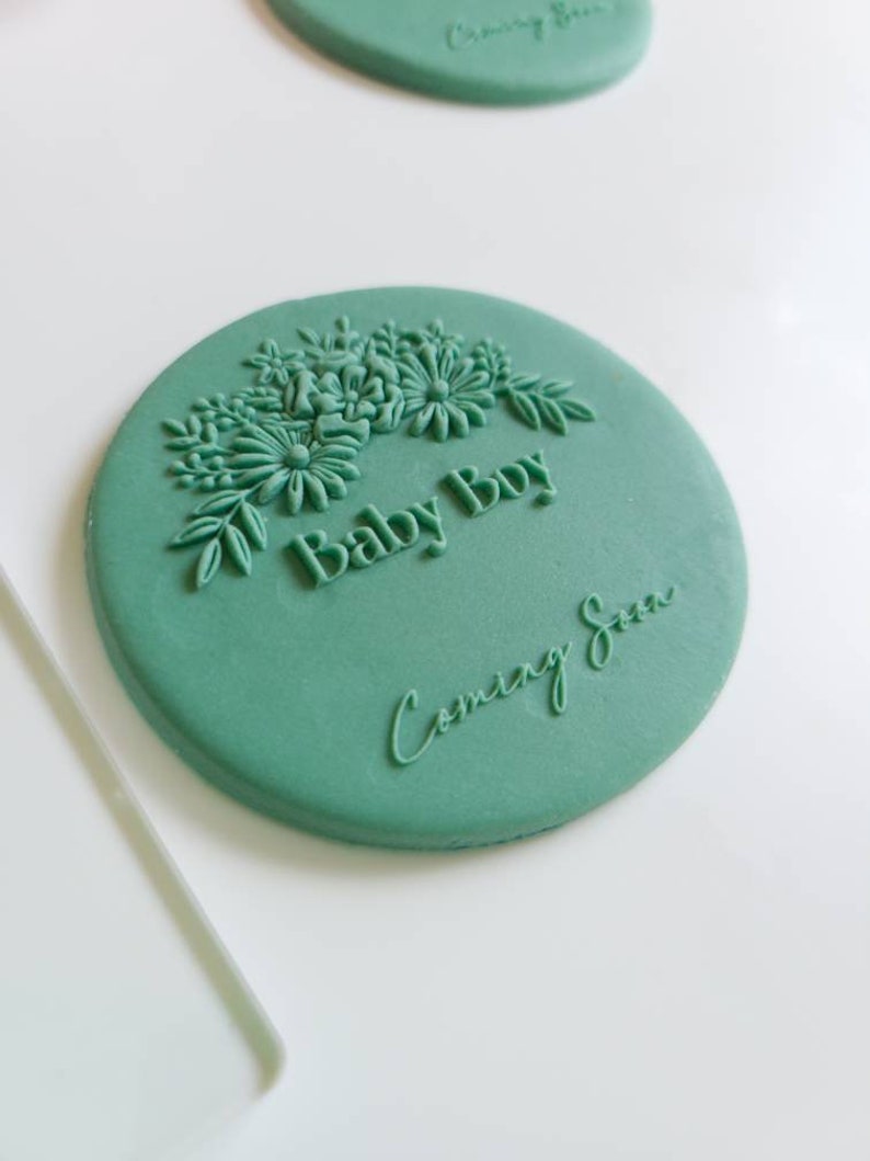 May include: A green round cake topper with a floral design and the text "Baby Boy Coming Soon".