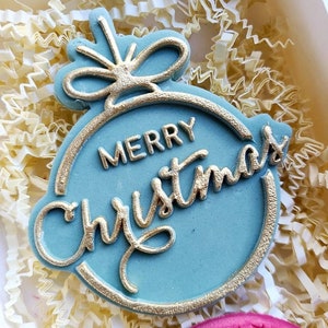 Op de afbeelding: Een blauwe en gouden kerstbal met de tekst "Merry Christmas" erop.