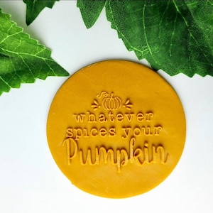 Op de afbeelding: Een ronde, gele rubberen stempel met de tekst "whatever spices your pumpkin" en een kleine pompoenafbeelding.