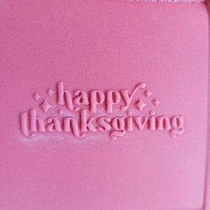 Op de afbeelding: Een roze achtergrond met de woorden "happy thanksgiving" in witte letters.
