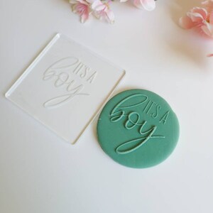 Op de afbeelding: Een transparante acryl stempel met de tekst "It's a boy" en een groene fondantkoekje met dezelfde tekst in reli&euml;f.