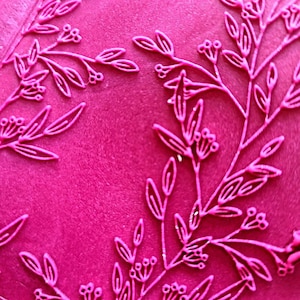 Op de afbeelding: Een close-up van een roze oppervlak met een delicaat, reliëf bloemenpatroon. Het patroon heeft kleine bladeren en bessen.