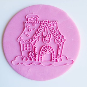Op de afbeelding: Roze siliconen gingerbread house stempel met een snoepstok, een swirl-ontwerp en een schoorsteen.