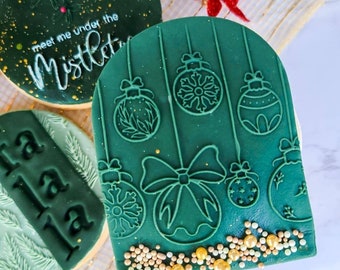 May include: Green Christmas cookie with a design of hanging ornaments and bows. The cookie is decorated with gold sprinkles.