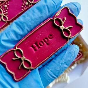 May include: A red and gold Christmas cracker with the word "Hope" written on it.