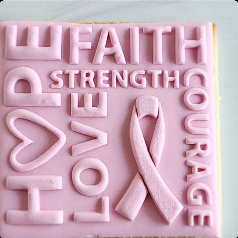 Pu&ograve; includere: Biscotto di zucchero rosa decorato con glassa rosa e in rilievo con le parole "HOPE", "LOVE", "FAITH", "STRENGTH", "COURAGE" e un nastro rosa.