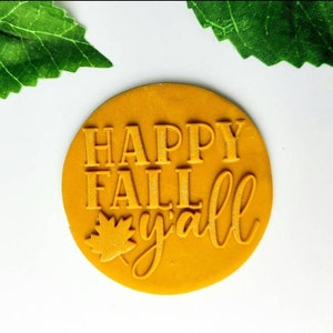 Op de afbeelding: Een ronde, gele siliconen stempel met de tekst "HAPPY FALL y'all" en een klein blaadjesontwerp.
