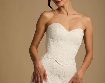 May include: A strapless white lace wedding dress. The bodice has a sweetheart neckline and a fitted waist. The skirt flows down to the floor. The dress is made of a delicate, textured lace fabric. The model is wearing the dress.