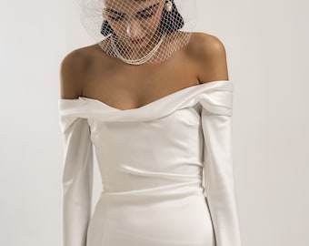 Könnte beinhalten: Ein weißes, schulterfreies Brautkleid mit langen Ärmeln und einer figurbetonten Silhouette. Das Kleid hat ein schlichtes, elegantes Design und ist perfekt für eine moderne Braut.