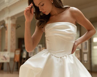 May include: A white strapless wedding dress with a fitted bodice and a flowing skirt. The dress is made of a smooth, satin fabric.
