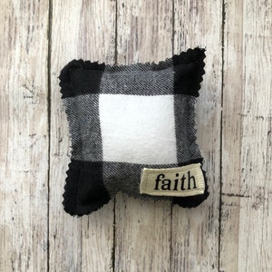 May include: A small black and white checkered pillow with a white center and a tan label that says "faith".