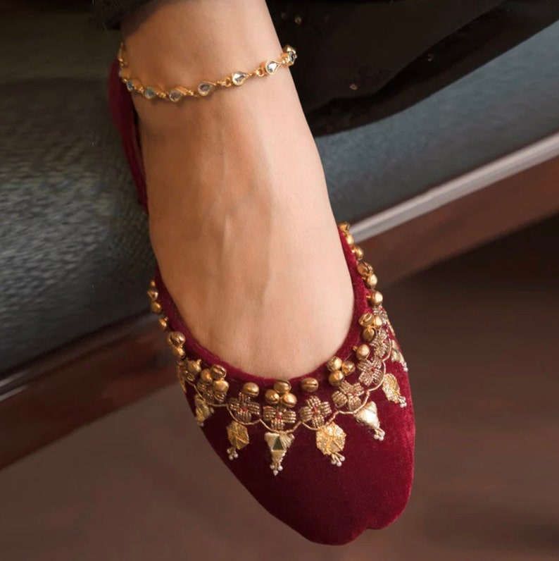 May include: Burgundy velvet flat shoes with gold embellishments and a beaded ankle bracelet.